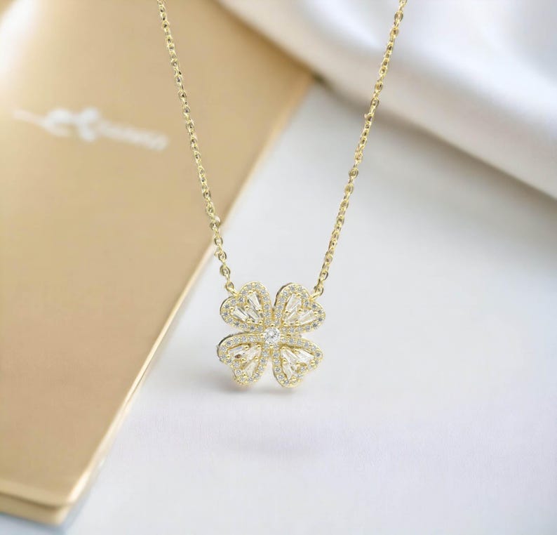 May include: A gold chain necklace with a four-leaf clover pendant encrusted with clear cubic zirconia stones.