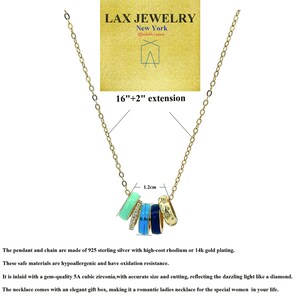 May include: Gold-toned necklace with a pendant featuring five colorful rings. The rings are in shades of blue, green, and gold, with one ring adorned with cubic zirconia. The chain is 16 inches with a 2-inch extension. The LAX JEWELRY logo is visible.