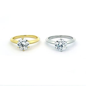 May include: Two engagement rings with a round brilliant cut diamond. The ring on the left is set in yellow gold, while the ring on the right is set in white gold.
