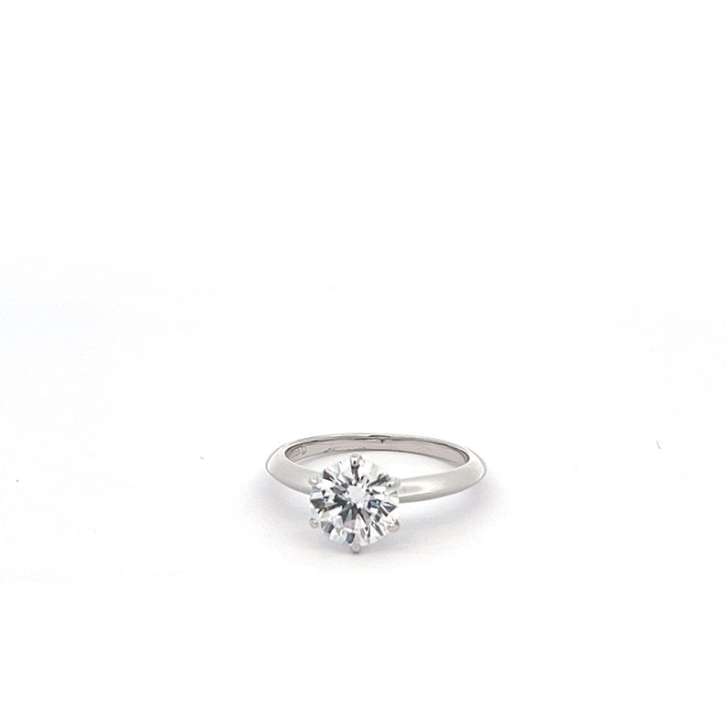 May include: A silver solitaire engagement ring with a round, clear diamond.