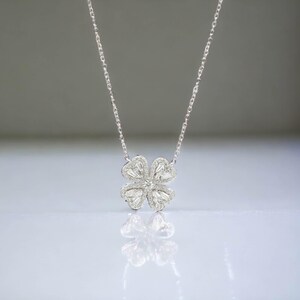 May include: A silver necklace with a four-leaf clover pendant encrusted with clear cubic zirconia stones.
