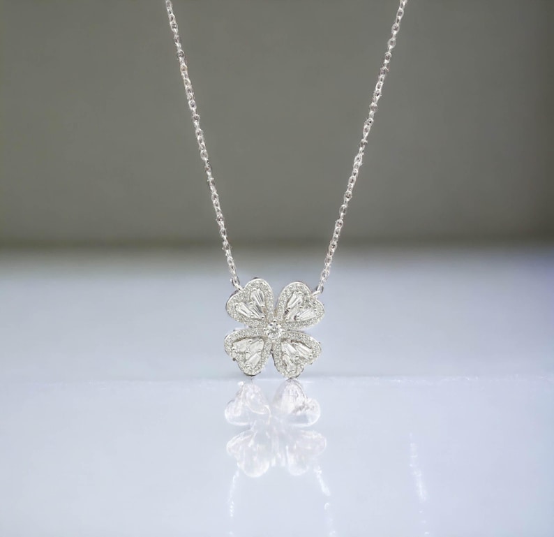 May include: A silver necklace with a four-leaf clover pendant encrusted with clear cubic zirconia stones.