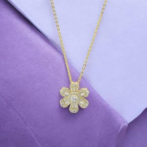 May include: A gold chain necklace with a flower pendant. The flower is made of clear cubic zirconia stones.