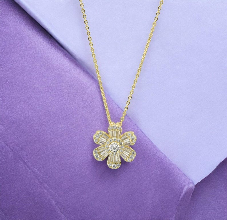 May include: A gold chain necklace with a flower pendant. The flower is made of clear cubic zirconia stones.