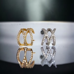 May include: Two ear cuffs, one gold and one silver, with a criss-cross design and clear cubic zirconia stones.