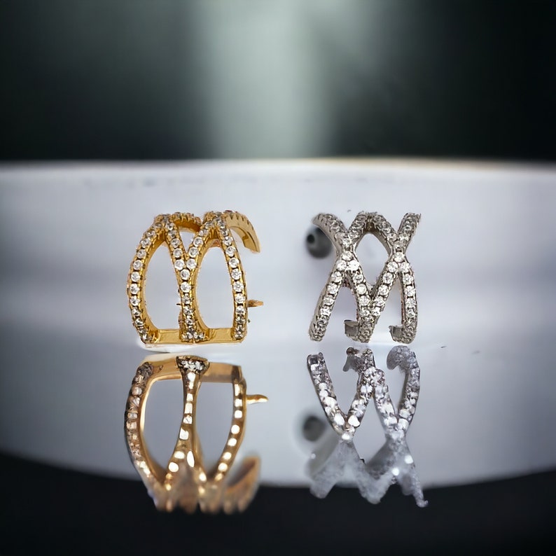 May include: Two ear cuffs, one gold and one silver, with a criss-cross design and clear cubic zirconia stones.