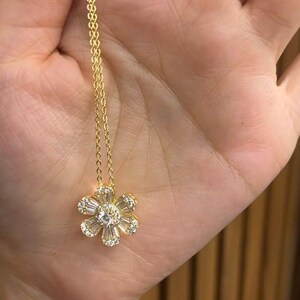 May include: A gold chain necklace with a delicate flower pendant featuring clear cubic zirconia stones.