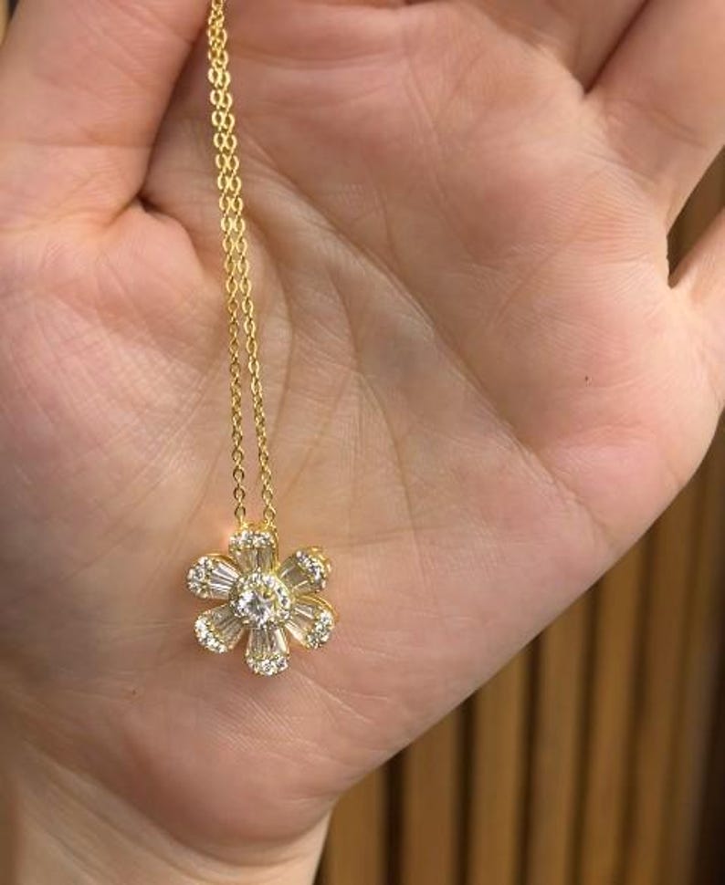 May include: A gold chain necklace with a delicate flower pendant featuring clear cubic zirconia stones.
