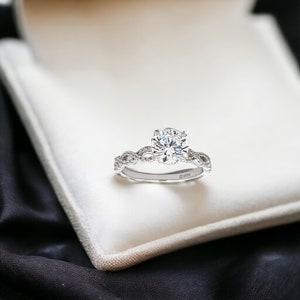 May include: A silver engagement ring with a large, round, clear diamond set in a braided band.
