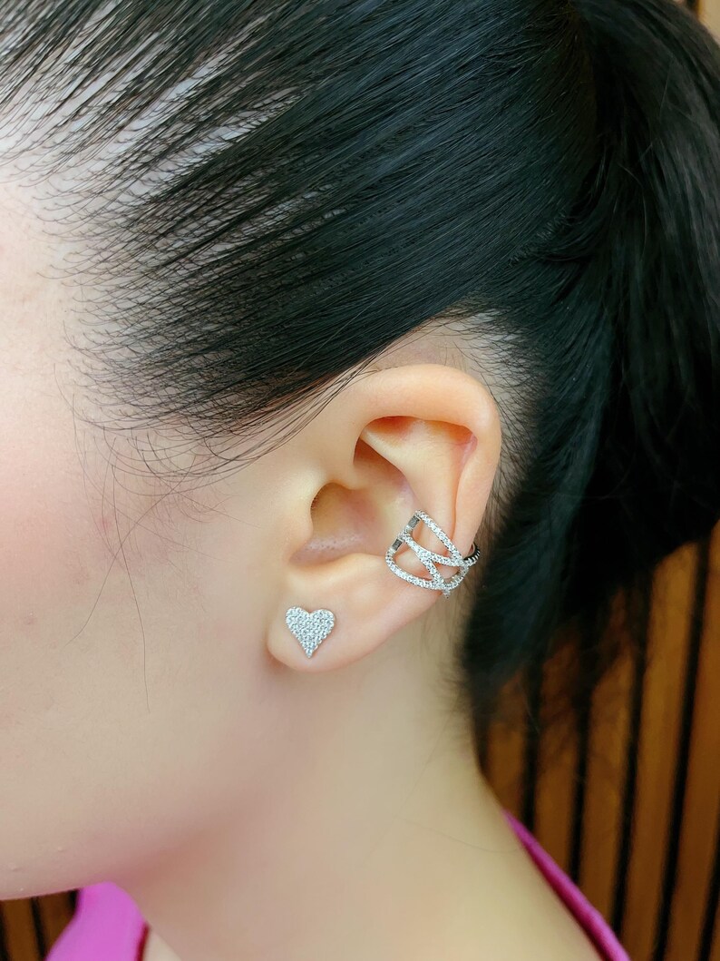 May include: A pair of silver earrings, one is a heart-shaped stud and the other is a triple-wrap ear cuff. Both earrings are adorned with sparkling clear cubic zirconia stones.