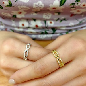May include: Two chain link rings, one silver and one gold, with small clear stones set into the links.