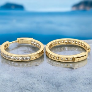 May include: A pair of gold hoop earrings with a row of clear cubic zirconia stones around the edge.