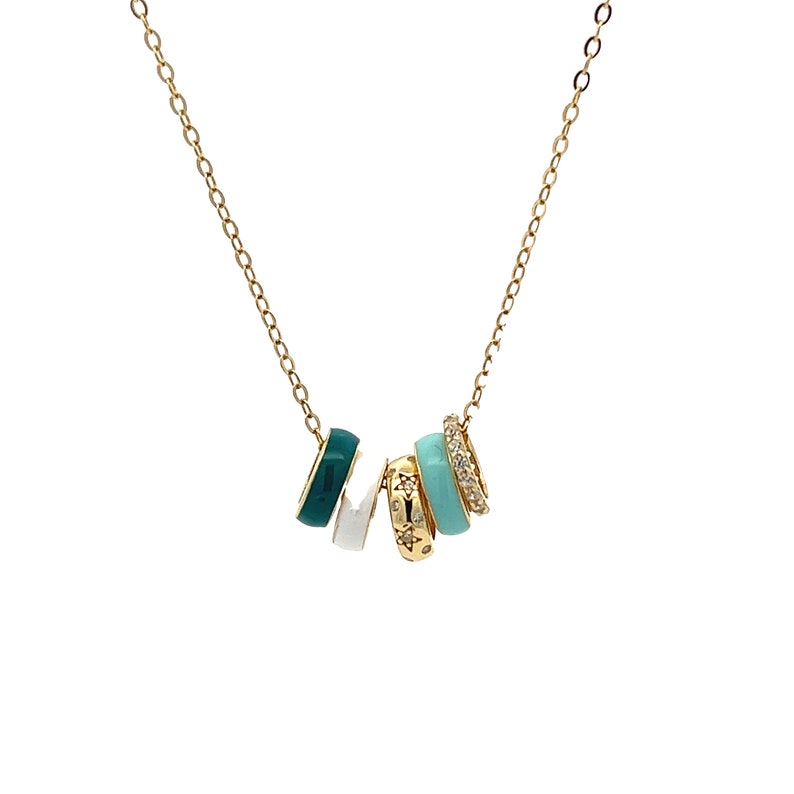 May include: A gold-colored necklace featuring five decorative rings. The rings are in various colors, including teal, white, and gold, with some adorned with small star and crystal accents. The necklace has a delicate chain.
