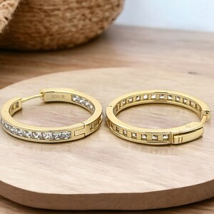 May include: Gold hoop earrings with a row of clear square-shaped stones around the edge.