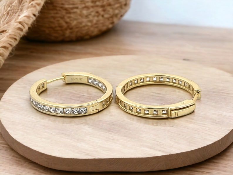 May include: Gold hoop earrings with a row of clear square-shaped stones around the edge.