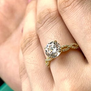 May include: A gold engagement ring with a large, round, clear diamond set in a twisted band.