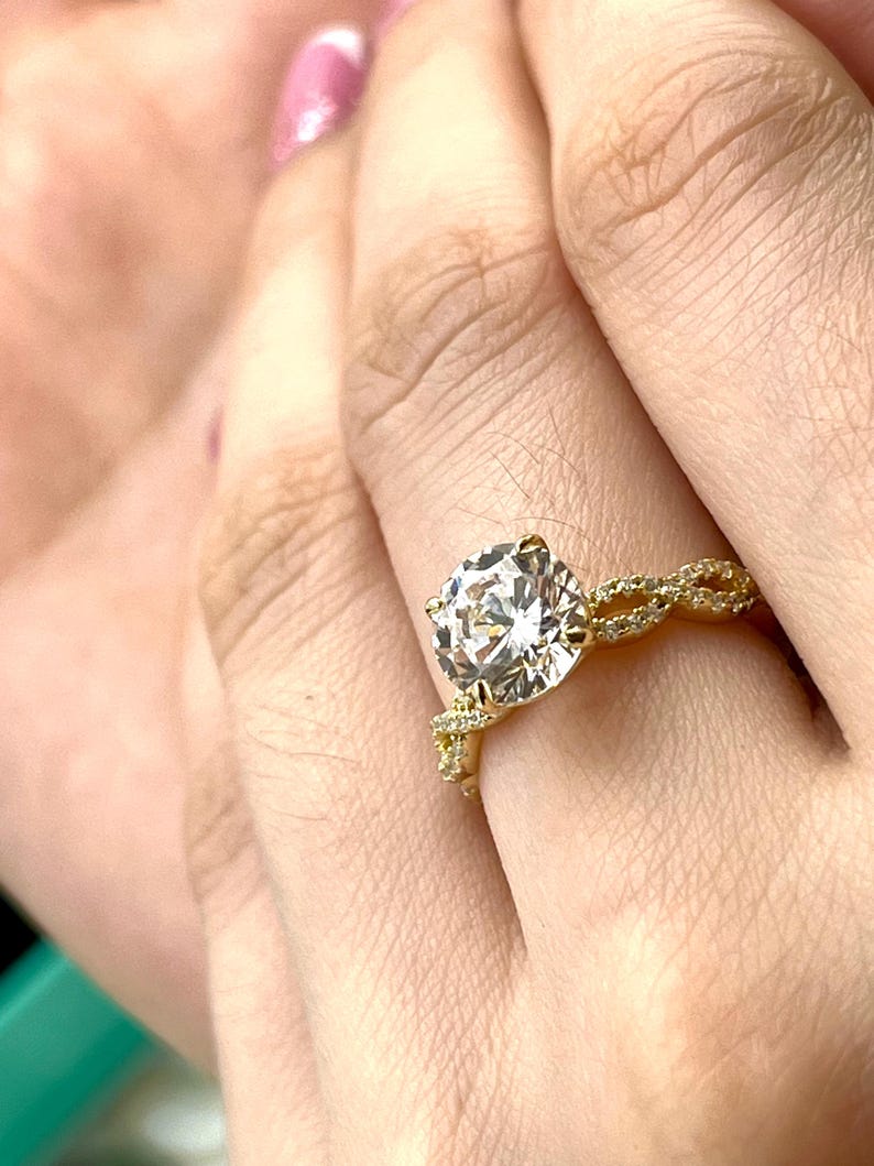 May include: A gold engagement ring with a large, round, clear diamond set in a twisted band.
