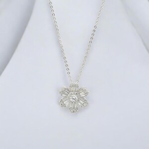 May include: A silver chain necklace with a flower pendant. The flower is made of small, clear stones and has a round center stone.