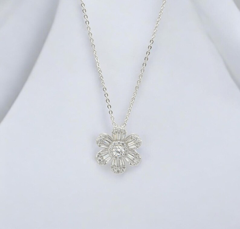 May include: A silver chain necklace with a flower pendant. The flower is made of small, clear stones and has a round center stone.