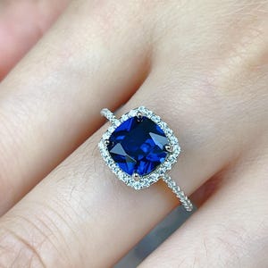 May include: A silver ring with a large, square-shaped blue sapphire surrounded by a halo of smaller diamonds.