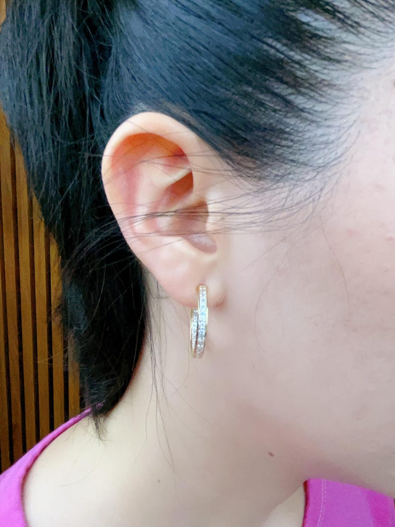 May include: A pair of gold hoop earrings with a row of small clear stones around the edge.