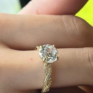 May include: A gold engagement ring with a large round diamond center stone and a braided band of smaller diamonds.