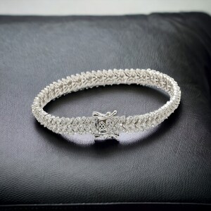May include: A silver tennis bracelet with a row of small, clear cubic zirconia stones.