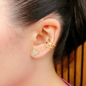 May include: A pair of gold earrings with clear cubic zirconia stones. One earring is a heart-shaped stud and the other is a curved ear cuff.