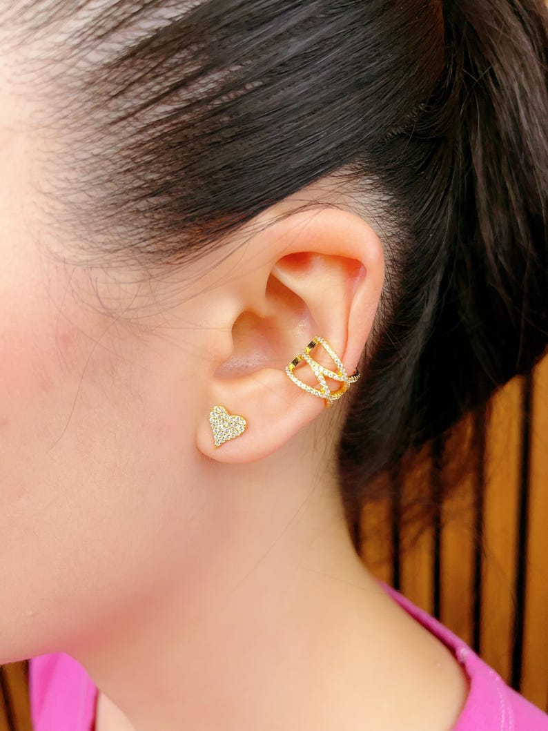 May include: A pair of gold earrings with clear cubic zirconia stones. One earring is a heart-shaped stud and the other is a curved ear cuff.
