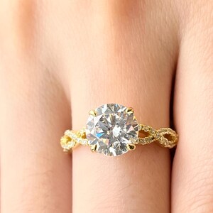 May include: A gold engagement ring with a large, round, clear diamond center stone. The band is a braided design with smaller diamonds.