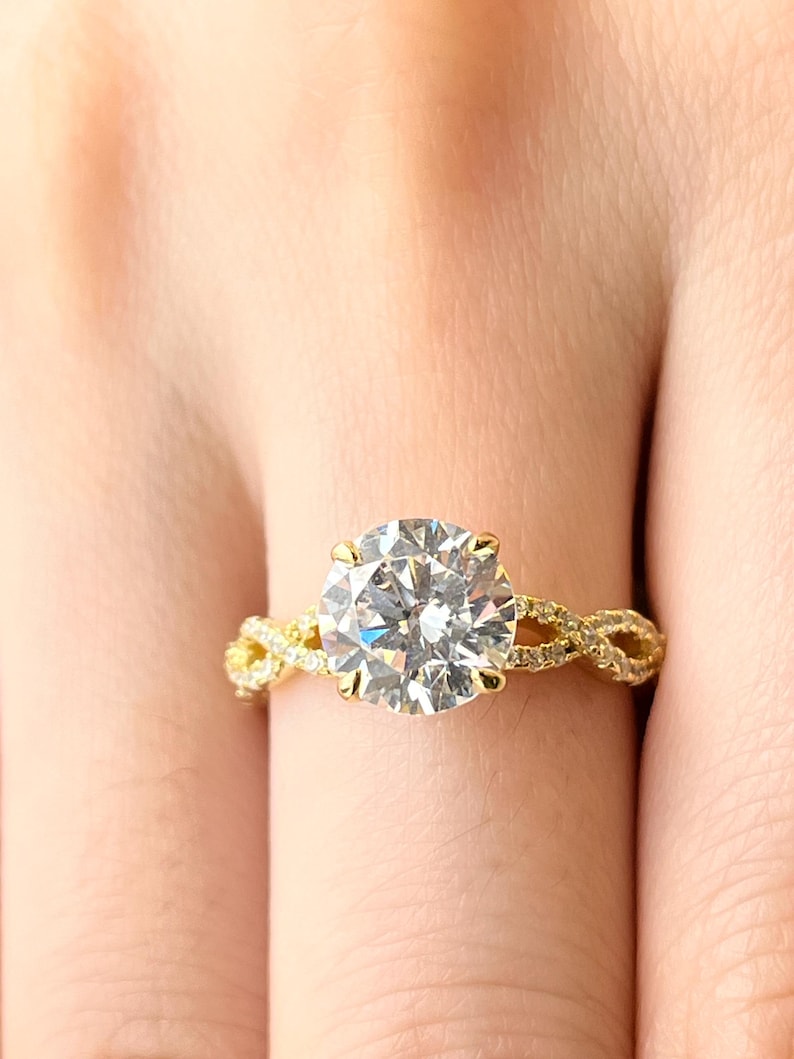 May include: A gold engagement ring with a large, round, clear diamond center stone. The band is a braided design with smaller diamonds.