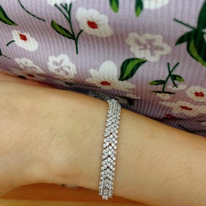 May include: A silver bracelet with a row of small, clear stones set in a chevron pattern.