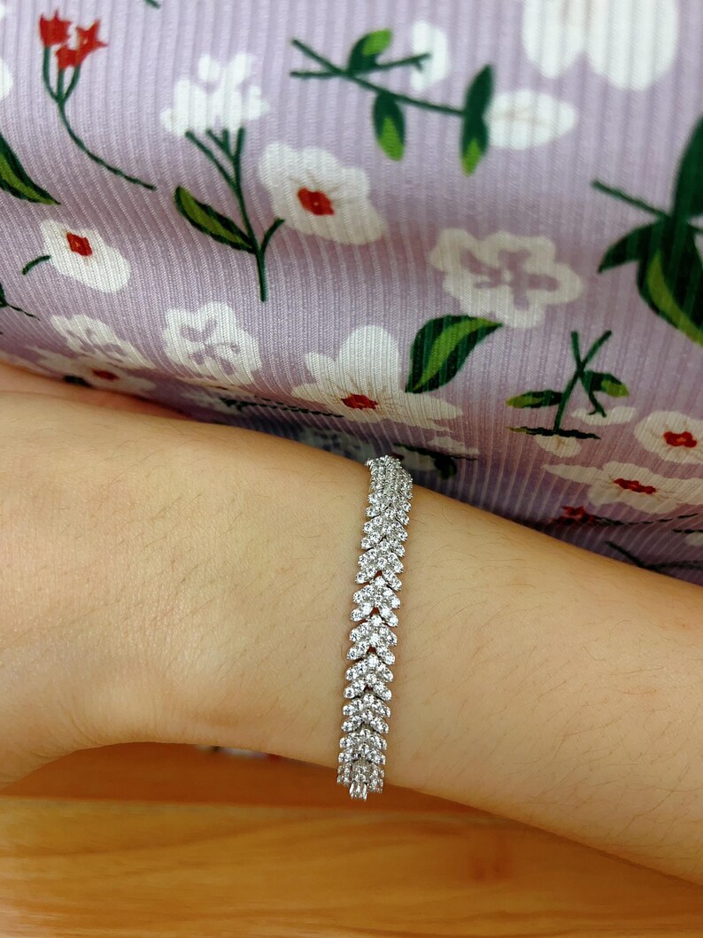 May include: A silver bracelet with a row of small, clear stones set in a chevron pattern.