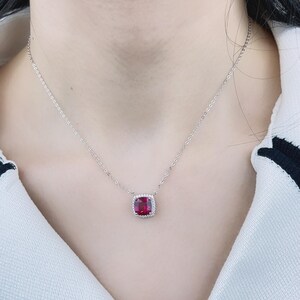 May include: A silver chain necklace with a red gemstone pendant. The pendant is surrounded by smaller clear gemstones.