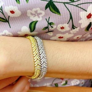 May include: Three gold and silver bracelets with a chevron design. The bracelets are made of metal and have small, clear stones that resemble diamonds.