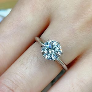 May include: A silver engagement ring with a large, round, clear diamond.