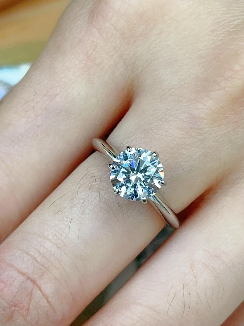 May include: A silver engagement ring with a large, round, clear diamond.