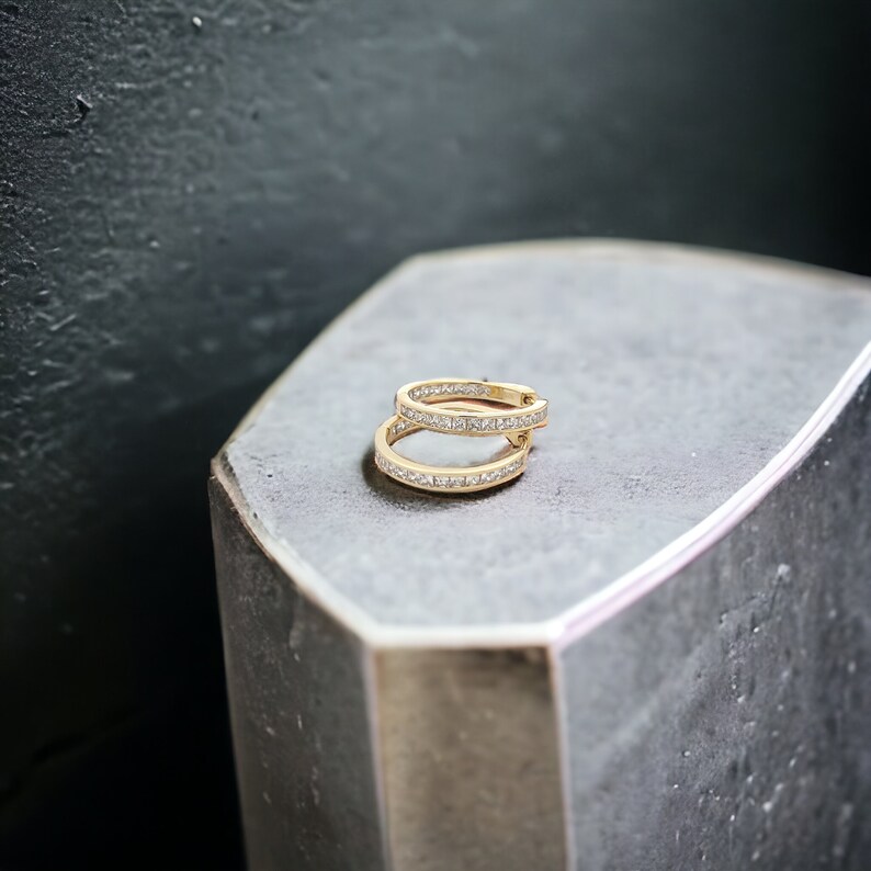 May include: A pair of gold hoop earrings with a row of small, clear cubic zirconia stones set in the band.