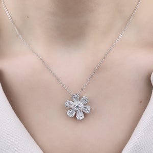 May include: A silver chain necklace with a flower-shaped pendant made of sparkling white diamonds.