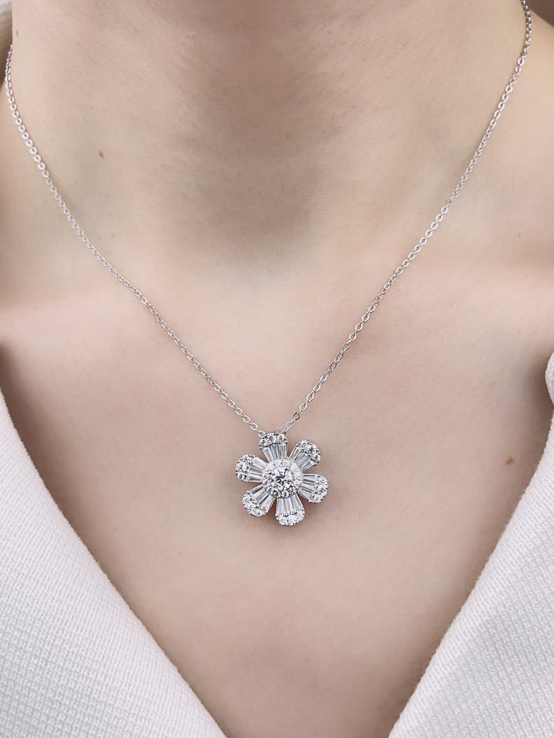May include: A silver chain necklace with a flower-shaped pendant made of sparkling white diamonds.