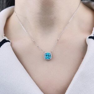 May include: A silver chain necklace with a square blue gemstone pendant surrounded by smaller clear gemstones.