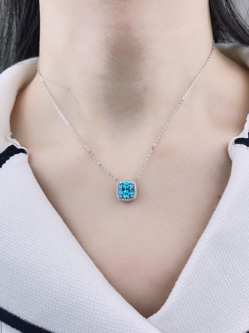 May include: A silver chain necklace with a square blue gemstone pendant surrounded by smaller clear gemstones.
