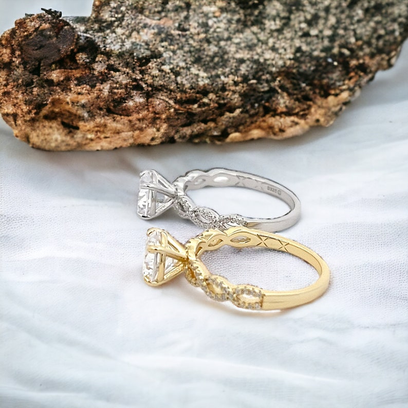 May include: Two engagement rings with a diamond center stone. The ring on the left is silver with a white gold band. The ring on the right is gold with a yellow gold band.