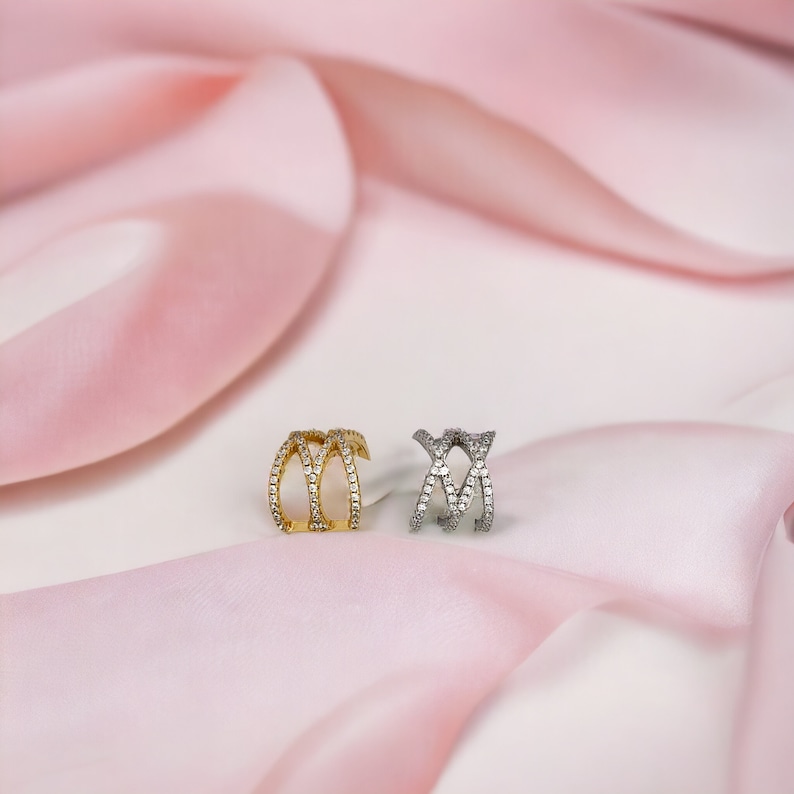 May include: Two ear cuffs with a criss-cross design, one is gold and the other is silver, both are set with clear cubic zirconia stones.