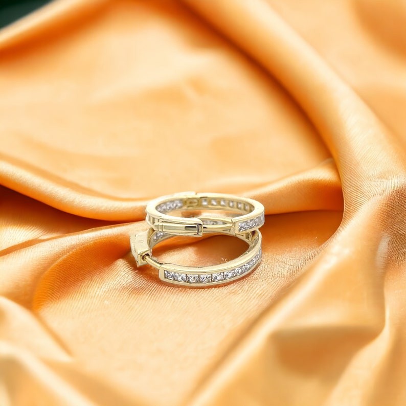 May include: A pair of gold hoop earrings with a row of small, clear cubic zirconia stones set in the band.
