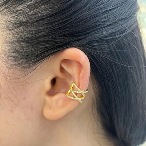 May include: Gold ear cuff with a geometric design featuring clear cubic zirconia stones.