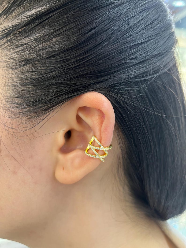 May include: Gold ear cuff with a geometric design featuring clear cubic zirconia stones.