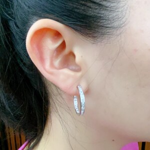 May include: Silver hoop earrings with a row of clear cubic zirconia stones around the edge.
