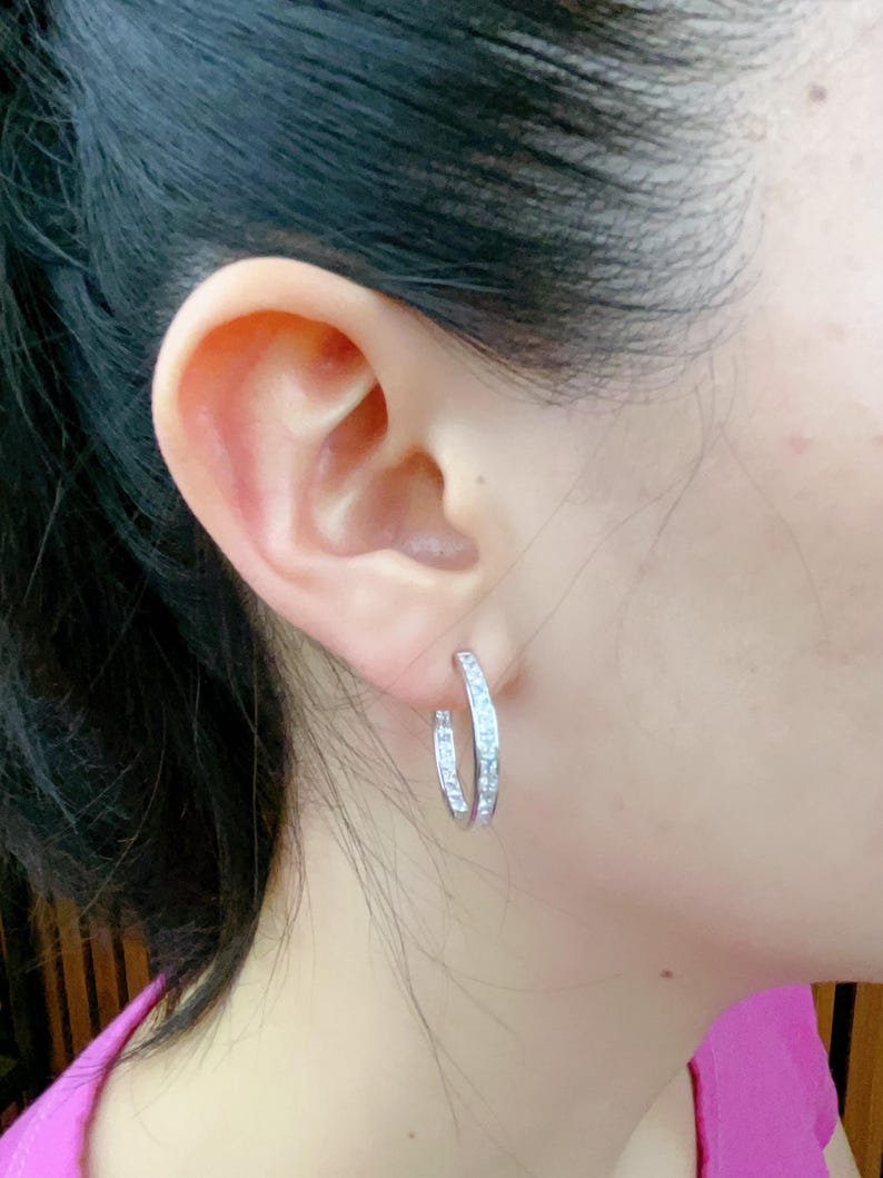 May include: Silver hoop earrings with a row of clear cubic zirconia stones around the edge.