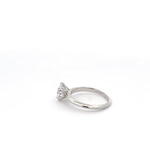 May include: A silver engagement ring with a round, clear diamond. The ring has a simple band and the diamond is set in a four-prong setting.